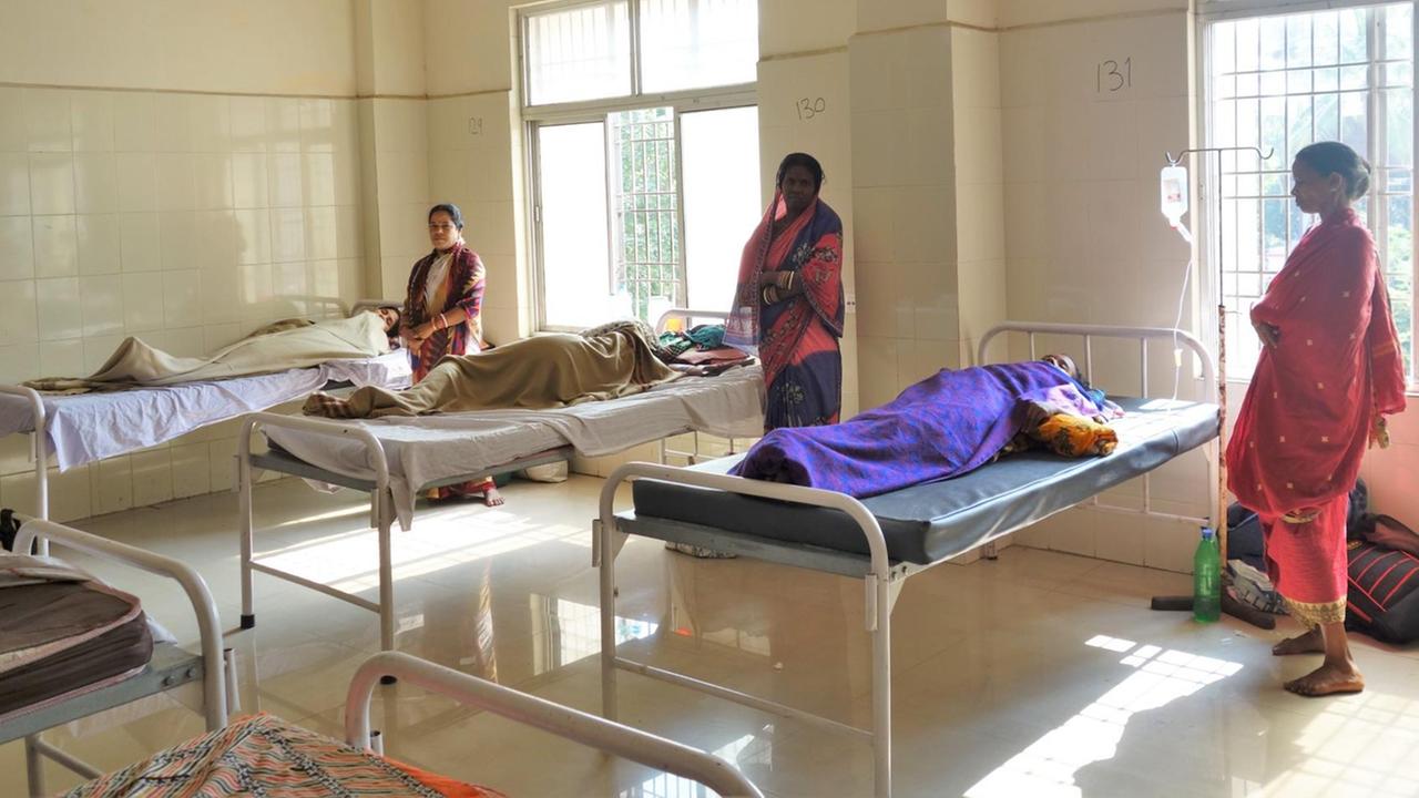Die Frauenstation des psychiatrischen Krankenhauses in Cuttack im Osten Indiens. Gefließte Wände, einfache Betten, Angehörige stehen um die liegenden Erkrankten.