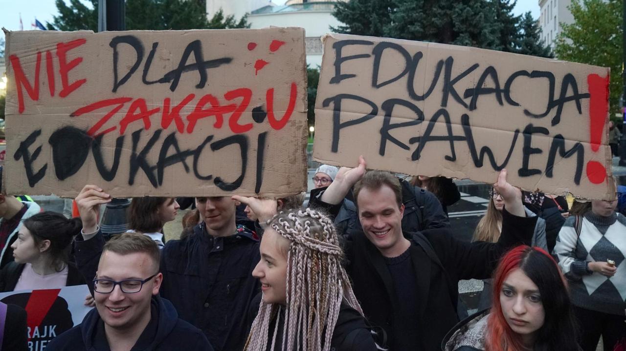 Menschen halten auf einer Demonstration in Warschau Plakate hoch mit polnischer Aufschrift.