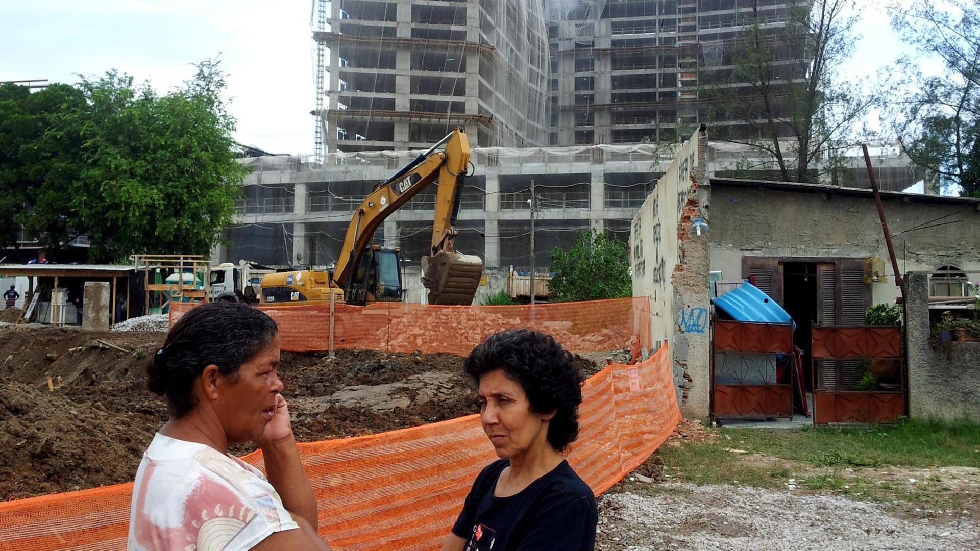 Dona Jane und Maria da Penha neben der Baustelle des Abwasserschachts (l.) und Janes Haus (r.), im Hintergrund ist das geplante Hotel zu sehen.