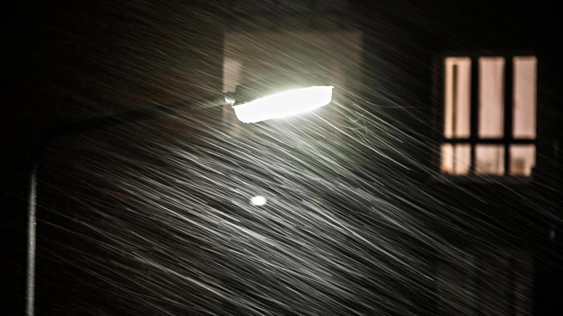 Ein Sturm treibt in der Nacht Schneeflocken an einer Straßenlaterne vorbei.