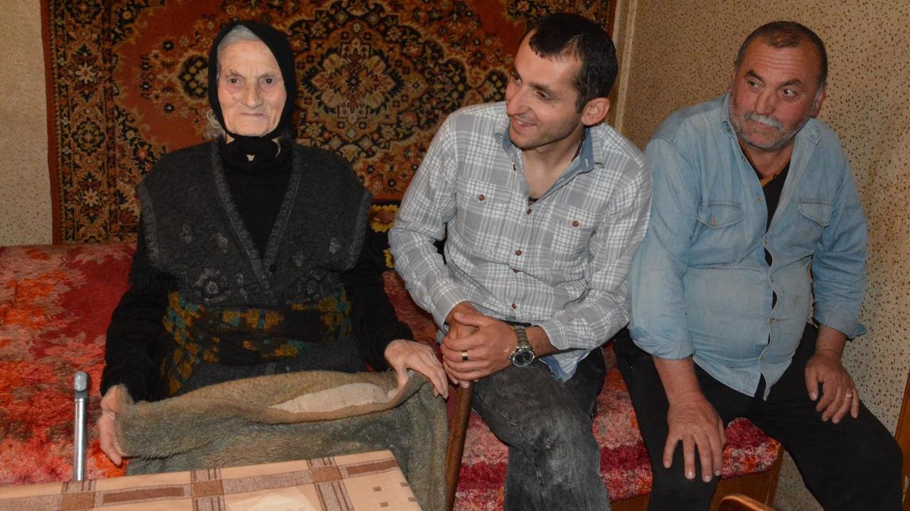 Großmutter, Sohn und Enkel in georgischer Provinz sitzen nebeneinander auf einer Couch.