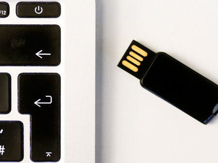 Großaufnahme eines USB-Sticks neben einer Laptop-Tastatur. Von der Tastatur sind nur sechs Tasten zu sehen, u.a. die Eingabe- und die Zurücktaste.