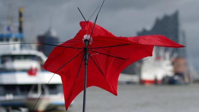 Sturm "Xavier" über Hamburg: An den Landungsbrücken geht ein Regenschirm im teils orkanartigen Wind zu Bruch.
