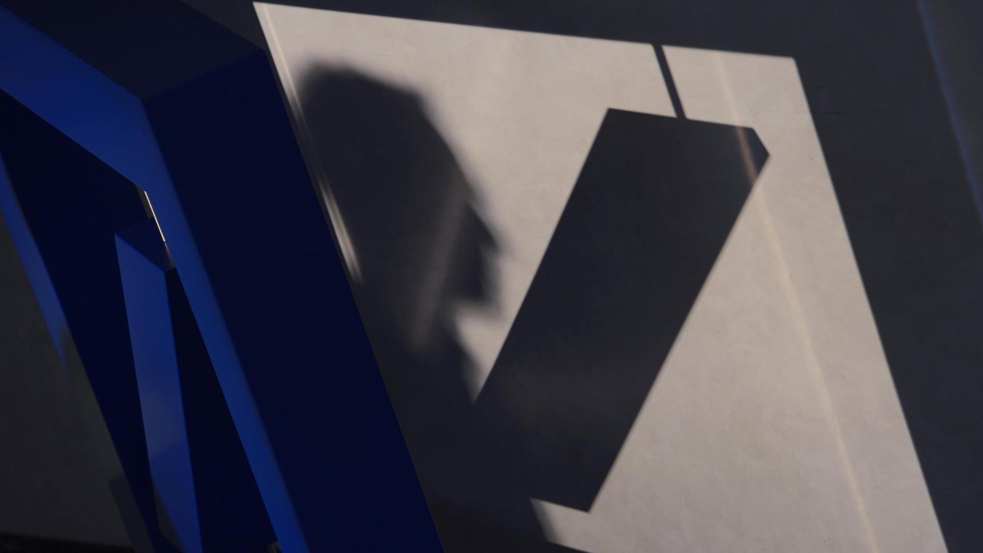 Die Schatten des Deutsche Bank-Logos und eines Mannes fallen auf eine Wand. Die Schatten des Deutsche Bank-Logos und eines Mannes fallen auf eine Wand.