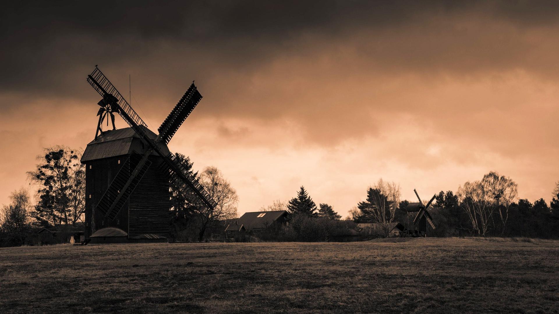 Zwei historische Windmühlen vor einem dramatisch gefärbten Himmel, im Vordergrund ist eine Wiese zu sehen. Zwei historische Windmühlen vor einem dramatisch gefärbten Himmel, im Vordergrund ist eine Wiese zu sehen.