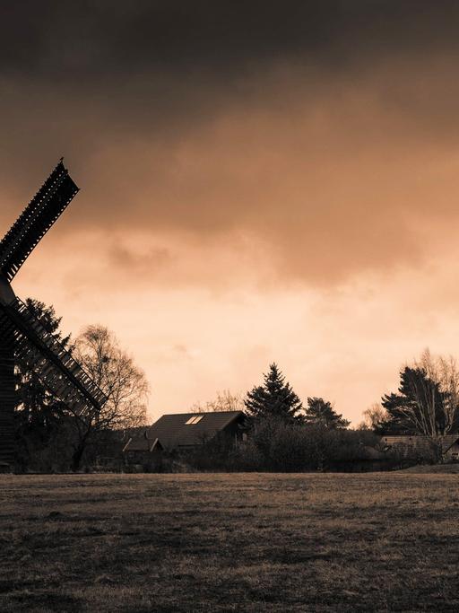 Zwei historische Windmühlen vor einem dramatisch gefärbten Himmel, im Vordergrund ist eine Wiese zu sehen.