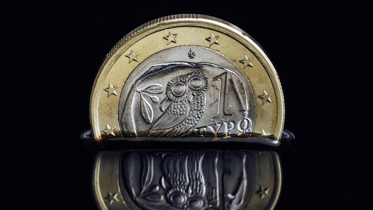 Die griechische Euro-Münze versinkt in schwarzer Flüssigkeit. Die griechische Euro-Münze versinkt in schwarzer Flüssigkeit.