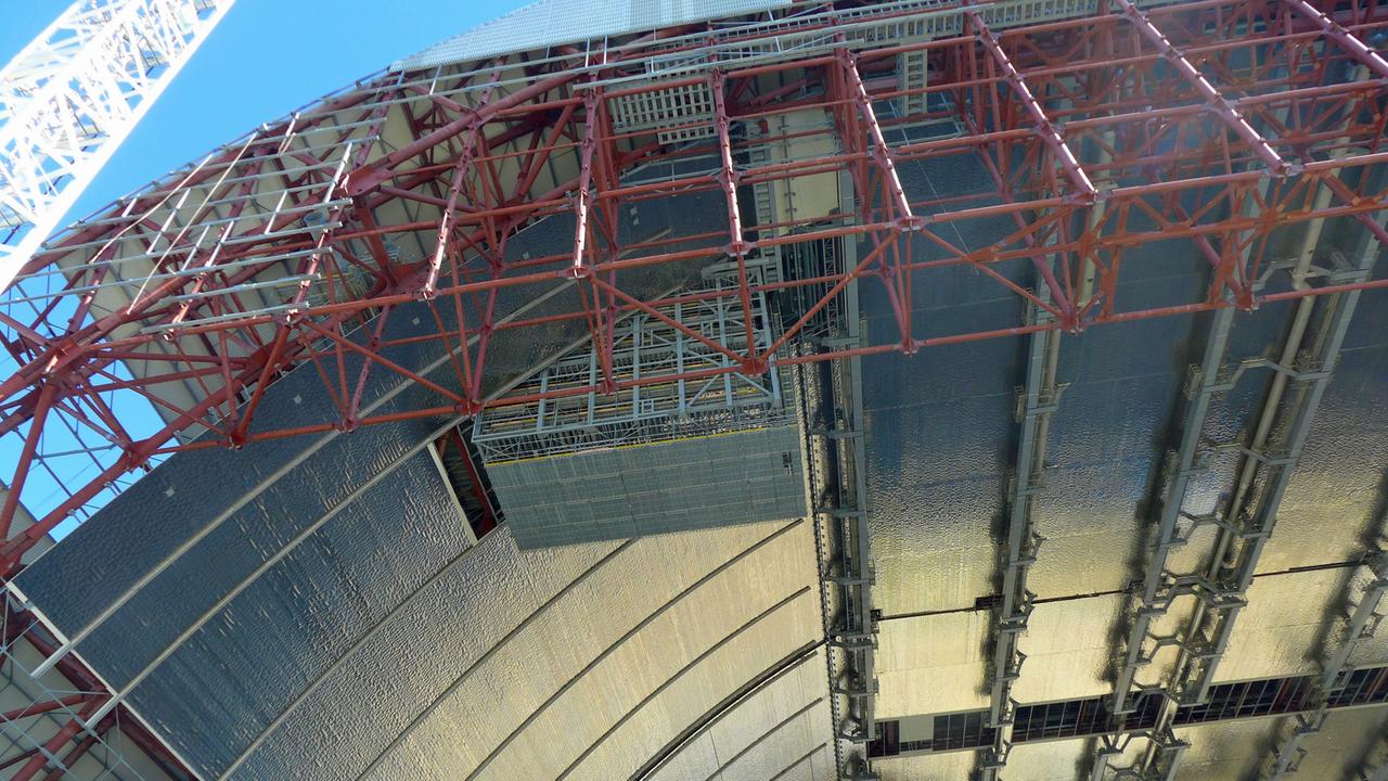 Hoch oben unter dem Dach des New Safe Confinements hängt bereits das Gerüst der Kanzel, von der aus Demontagearbeiten ferngesteuert ablaufen sollen Hoch oben unter dem Dach des New Safe Confinements hängt bereits das Gerüst der Kanzel, von der aus Demontagearbeiten ferngesteuert ablaufen sollen