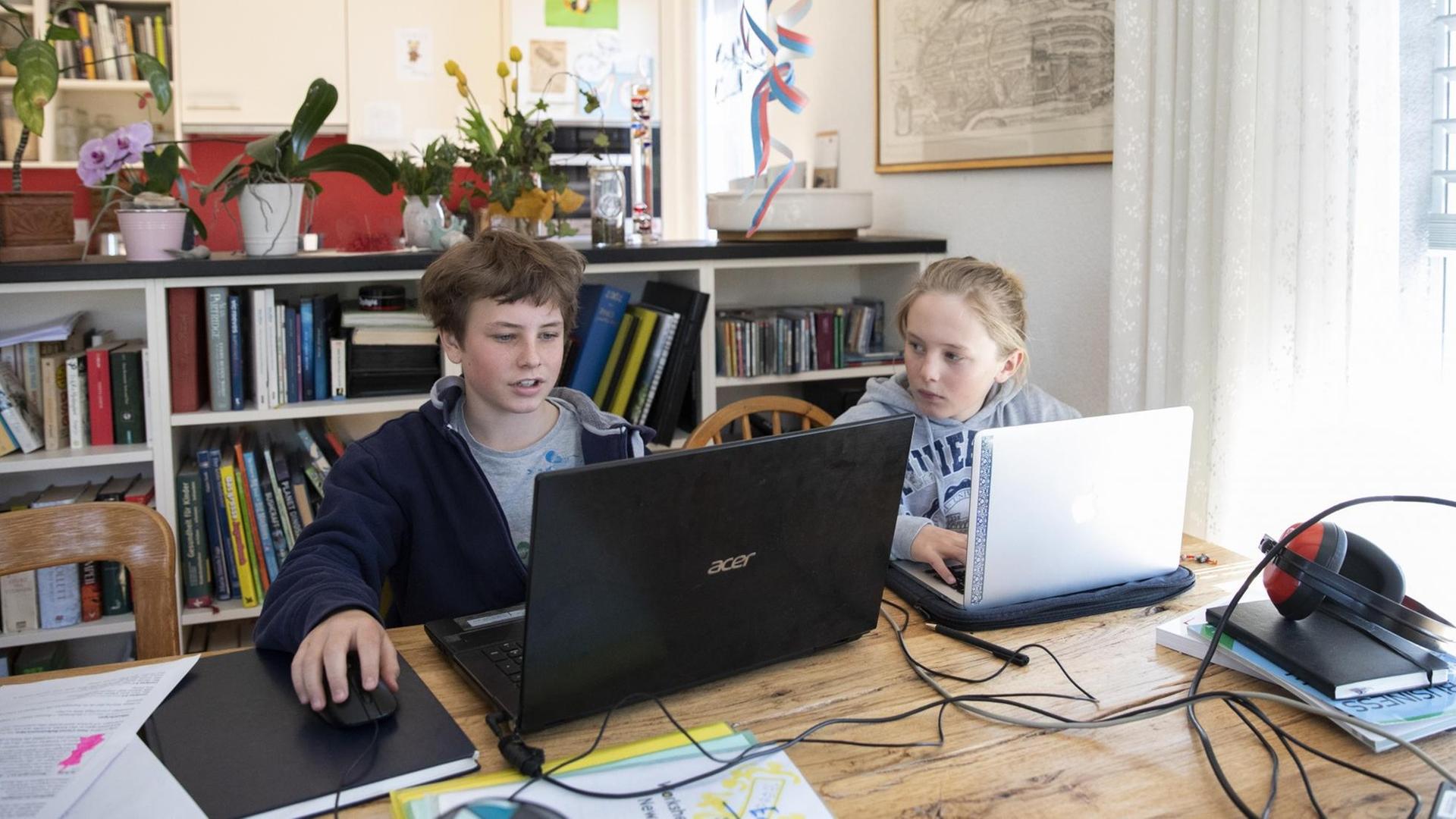 Zwei Jugendliche sitzen in einem Wohnzimmer vor Laptops und machen Hausaufgaben. Zwei Jugendliche sitzen in einem Wohnzimmer vor Laptops und machen Hausaufgaben.