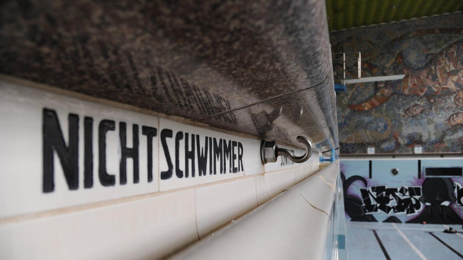 Blick auf ein leeres Schwimmbadbecken. Auf der linken Seite des Bildes dominiert der Schriftzug "Nichtschwimmer" am Beckenrand. Blick auf ein leeres Schwimmbadbecken. Auf der linken Seite des Bildes dominiert der Schriftzug "Nichtschwimmer" am Beckenrand.