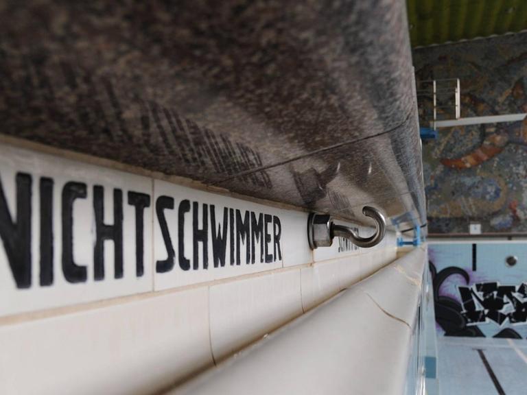 Blick auf ein leeres Schwimmbadbecken. Auf der linken Seite des Bildes dominiert der Schriftzug "Nichtschwimmer" am Beckenrand.