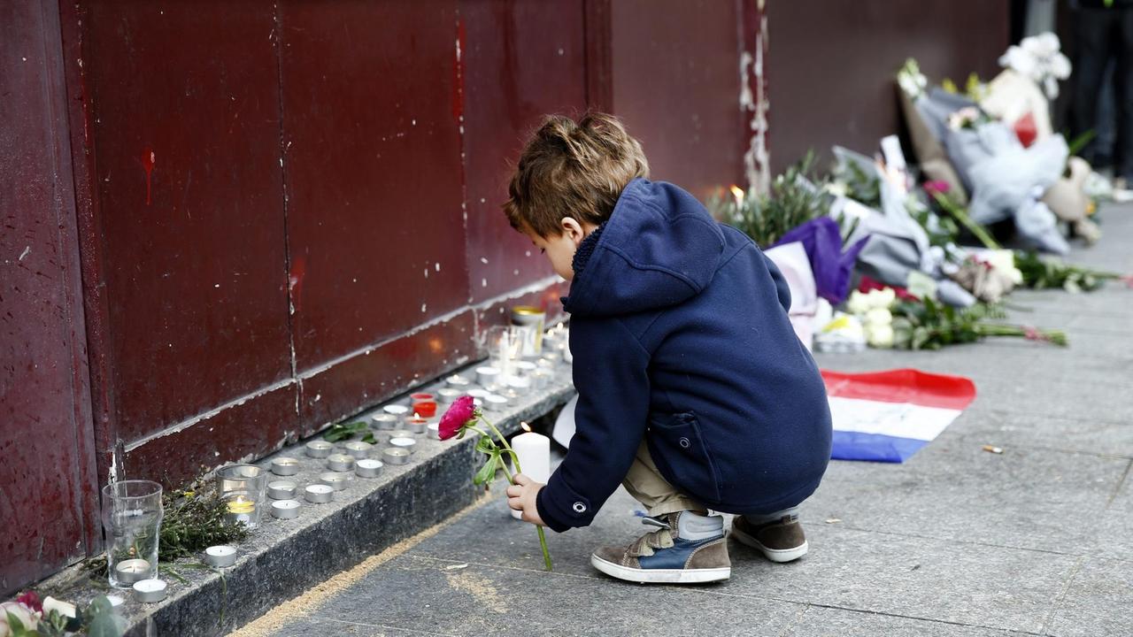 Ein kleiner Junge legt vor dem Carillon Cafe, einer der Anschlagsorte in Paris, Blumen nieder.