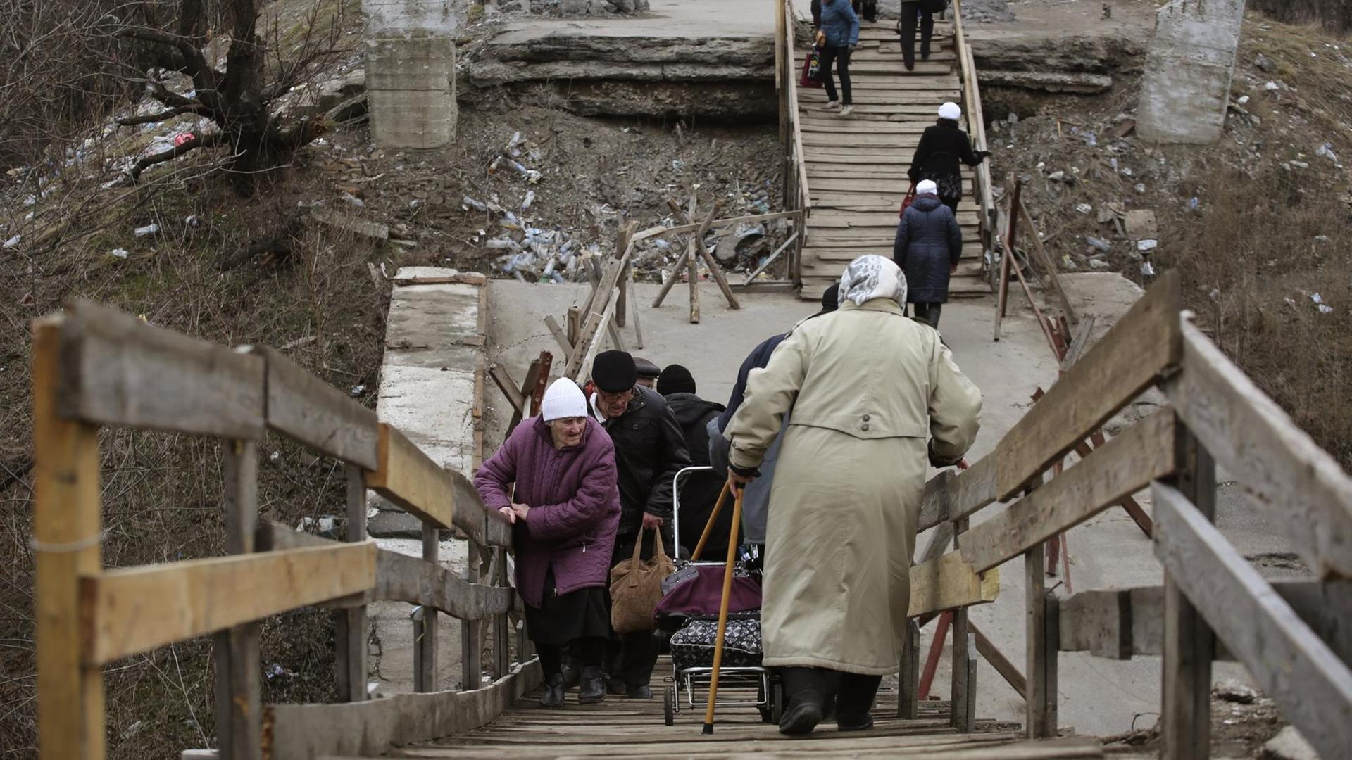 Die Menschen überqueren eine zerstörte Brücke in die Ukraine-kontrollierten Gebiet an einem Kontrollpunkt, der von pro-russischen Rebellen in Stanytsia Luhanska, Region Lugansk, am 7. März 2017 bewacht wird. Die Menschen überqueren eine zerstörte Brücke in die Ukraine-kontrollierten Gebiet an einem Kontrollpunkt, der von pro-russischen Rebellen in Stanytsia Luhanska, Region Lugansk, am 7. März 2017 bewacht wird.