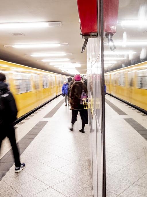 Eine U-Bahn fährt in den U-Bahnhof ein, die Szenerie spiegelt sich in einer Glasscheibe.
