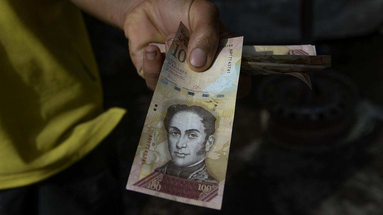 Ein Mann in Caracas hält einen 100-Bolivar-Schein.