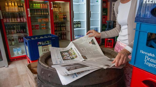 Eine Frau steht im Kölner Kiosk "Brigittes Büdchen" an einem Tisch und blättert in einer Lokalzeitung.