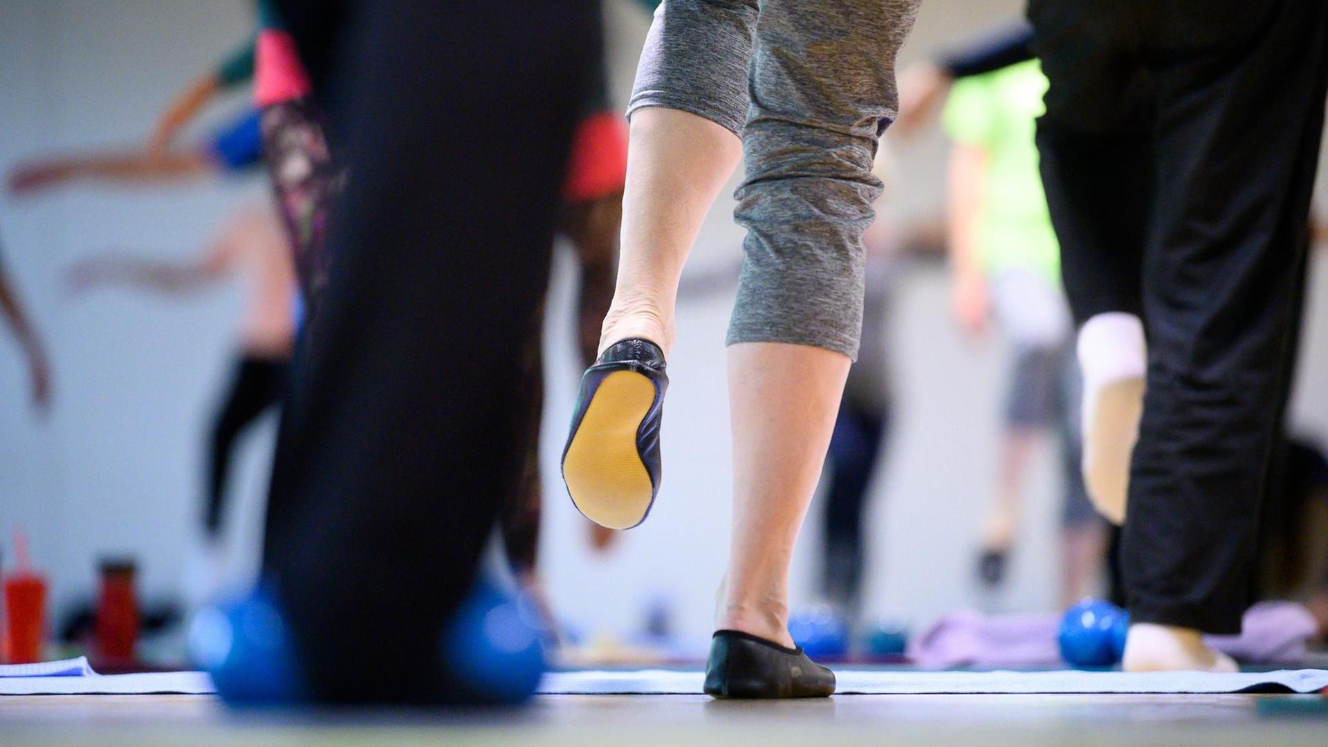 Teilnehmerinnen und Teilnehmer machen während einer Sportstunde für Menschen ab 60 eine Gleichgewichtsübung.