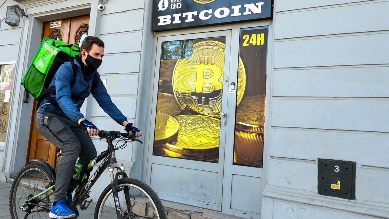 Ein Radfahrer mit Mundschutz fährt an einem Bitcoin-Wechsel-Laden in Krakau vorbei. Ein Radfahrer mit Mundschutz fährt an einem Bitcoin-Wechsel-Laden in Krakau vorbei.