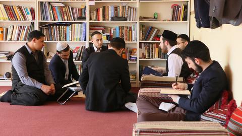 Schüler einer privaten Ergänzungsschule des Instituts Buhara in Berlin, das islamische Theologen ausbildet, sitzen in einem Klassenraum vor einem Bücherregal.