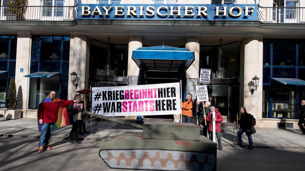 Demonstranten vom Aktionsbündnis "Gegen die Münchner Sicherheitskonferenz" stehen am 15.02.2017 mit Plakaten und einem Panzer aus Pappe vor dem Hotel "Bayerischer Hof". Demonstranten vom Aktionsbündnis "Gegen die Münchner Sicherheitskonferenz" stehen am 15.02.2017 mit Plakaten und einem Panzer aus Pappe vor dem Hotel "Bayerischer Hof".