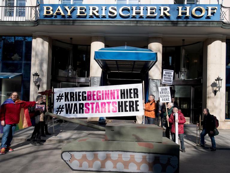 Demonstranten vom Aktionsbündnis "Gegen die Münchner Sicherheitskonferenz" stehen am 15.02.2017 mit Plakaten und einem Panzer aus Pappe vor dem Hotel "Bayerischer Hof".