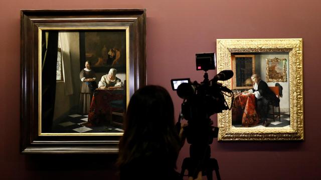 Sie sehen einen Journalisten, der das Gemälde "Briefschreiberin und Dienstmagd" von Vermeer filmt.