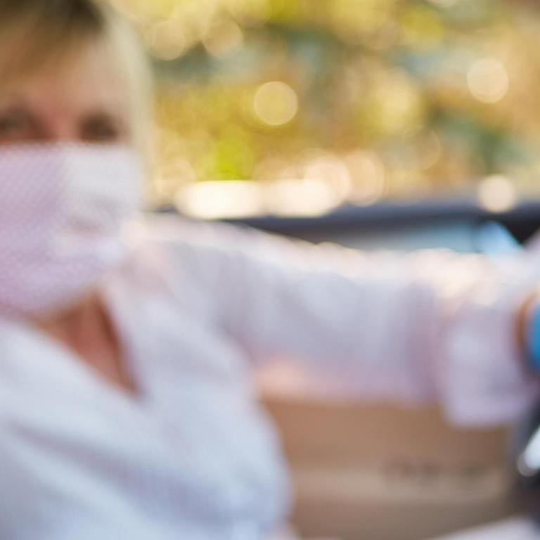 Frau im Auto mit Mundschutz und Desinfektionsmittel gegen Coronavirus oder mit Reizgas zur Selbstverteidigung | Verwendung weltweit
