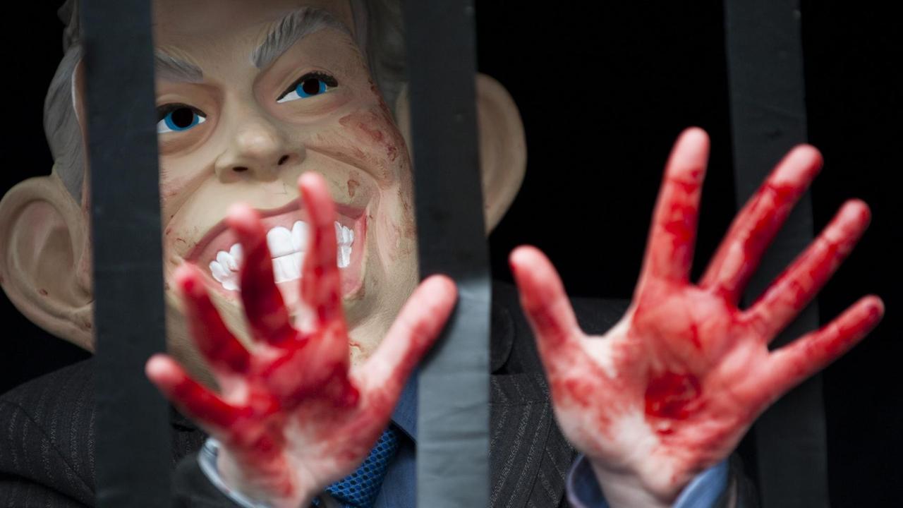 Bei einer Demonstration in London am 29. Januar 2010 steht ein Demonstrant mit einer Maske mit dem Konterfei des ehemaligen britischen Premiers Tony Blair hinter einem Gitter. Dabei zeigt er blutverschmierte Hände.