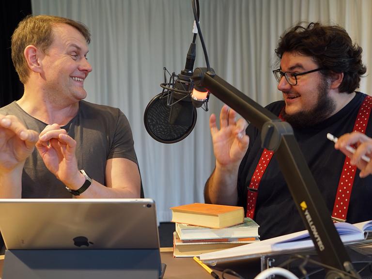 Devid Striesow und Axel Ranisch ahmen gestikulierend Dirigenten nach.