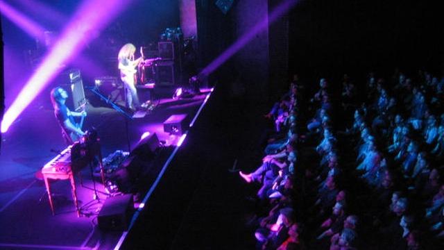 Zuhörer sitzen auf Stühlen vor der Bühne, auf der Steven Wilson mit seiner Band spielt.