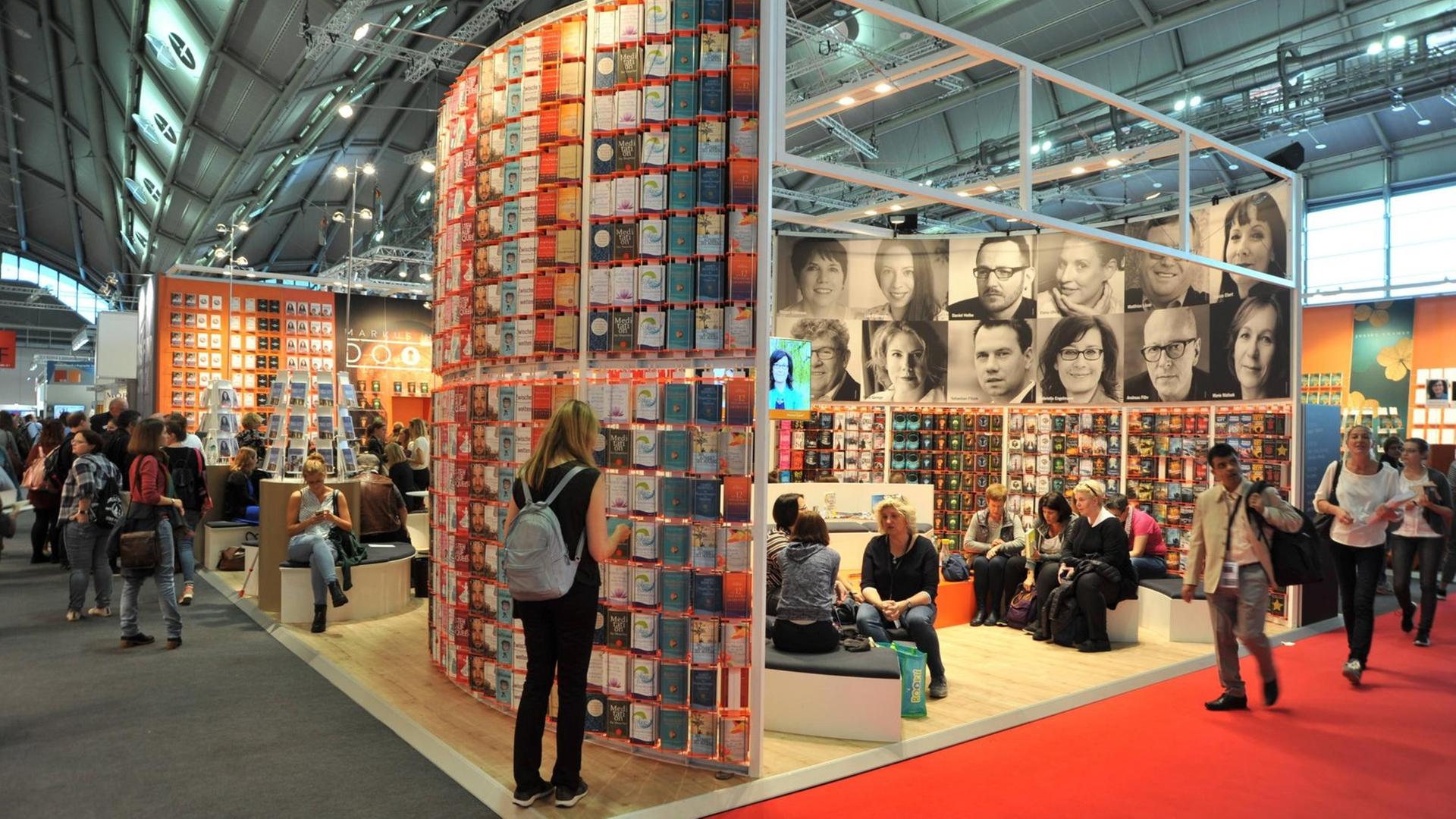 Besucherinnen und Besucher gehen zwischen den Messe-Ständen mit vielen Büchern entlang. Besucherinnen und Besucher gehen zwischen den Messe-Ständen mit vielen Büchern entlang.