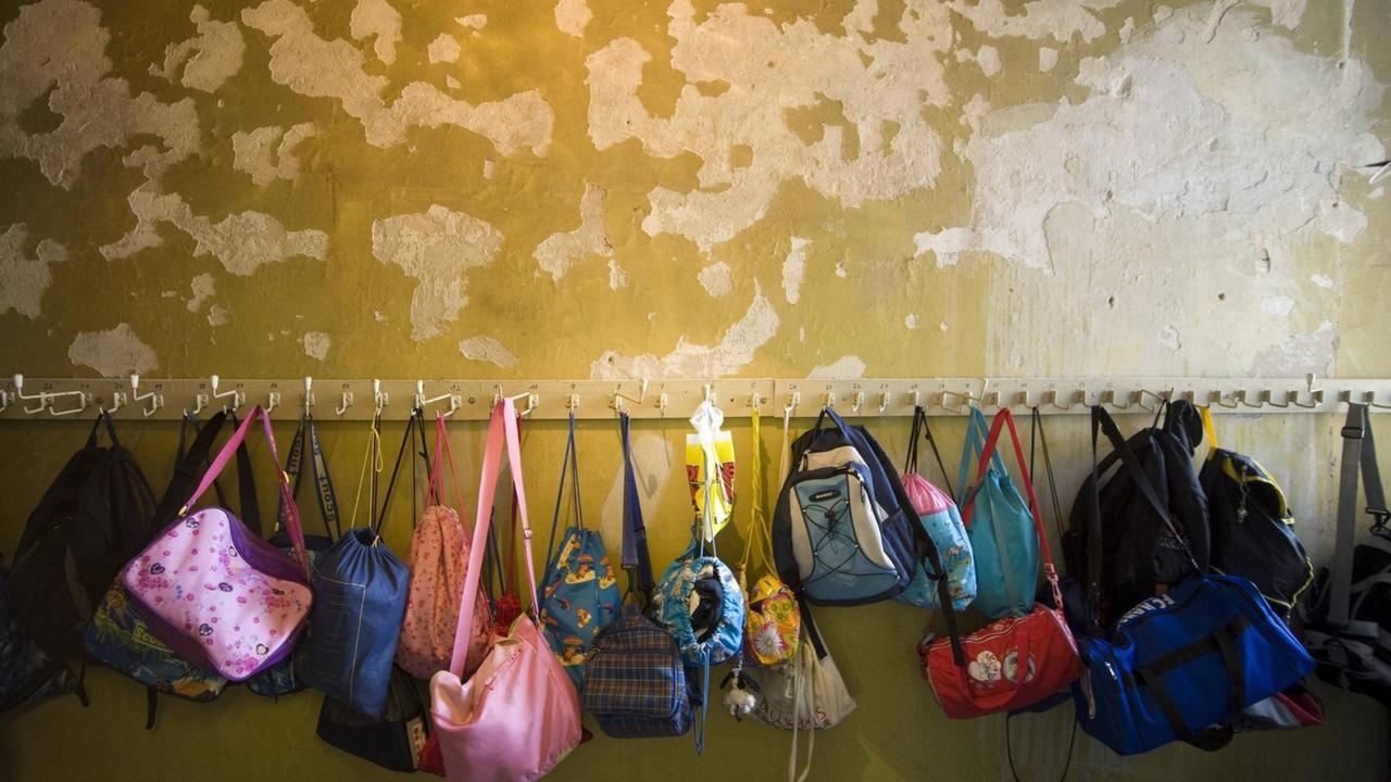 An einer Schulgarderobe hängen Taschen und Rucksäcke von den Kindern.