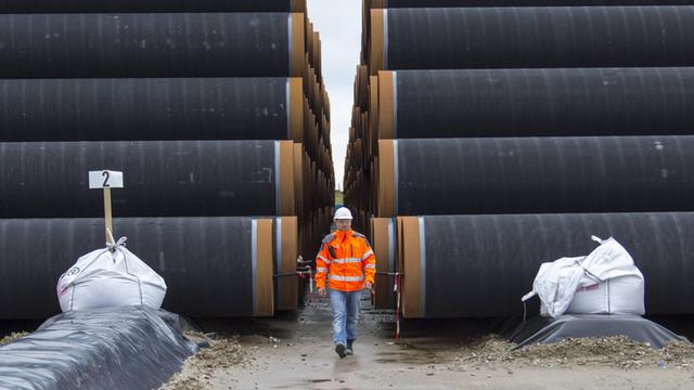 Ein Mann mit Schutzweste und Helm läuft im Fährhafen Sassnitz-Mukran auf Rügen zwischen zwei zu Türmen gestapelten Rohren für die geplante Gaspipeline Nord Stream 2 hindurch.
