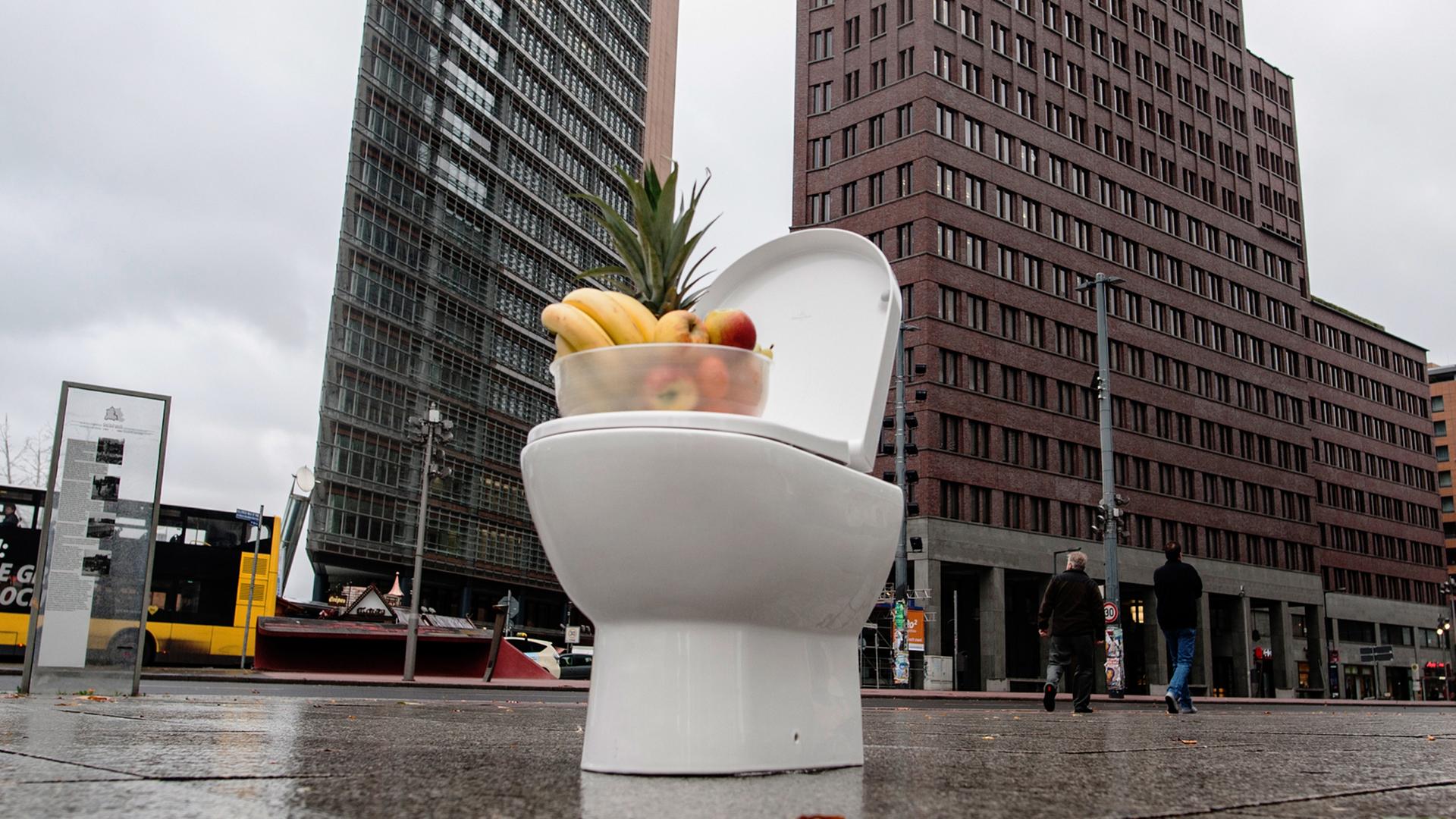 Eine Toilette mit einem Obstkorb steht auf einem großen Platz. Eine Toilette mit einem Obstkorb steht auf einem großen Platz.