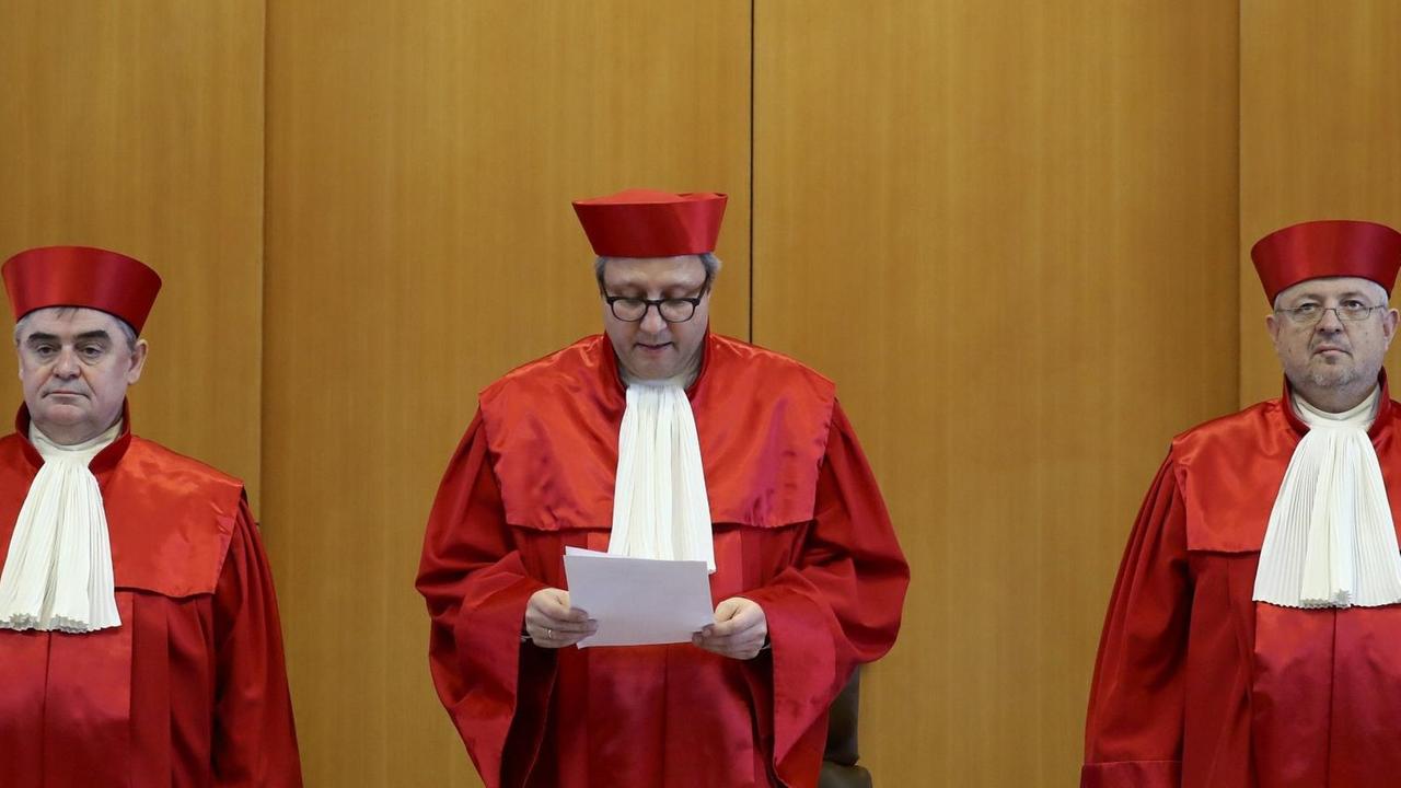 Die drei Richter stehen nebeneinander; Voßkuhle verliest gerade das Urteil, das er in den Händen hält.