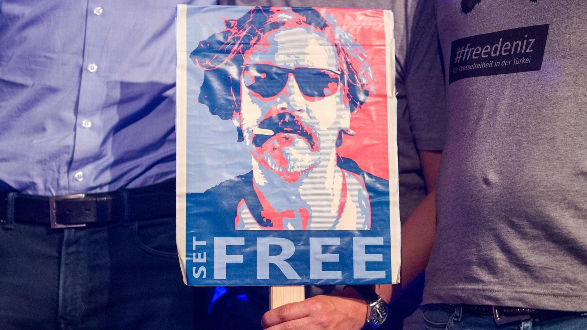 Das Archivbild zeigt ein Schild mit der Aufschrift "Free" und einem Foto des inhaftierten Journalisten Deniz Yücel. Das Archivbild zeigt ein Schild mit der Aufschrift "Free" und einem Foto des inhaftierten Journalisten Deniz Yücel.