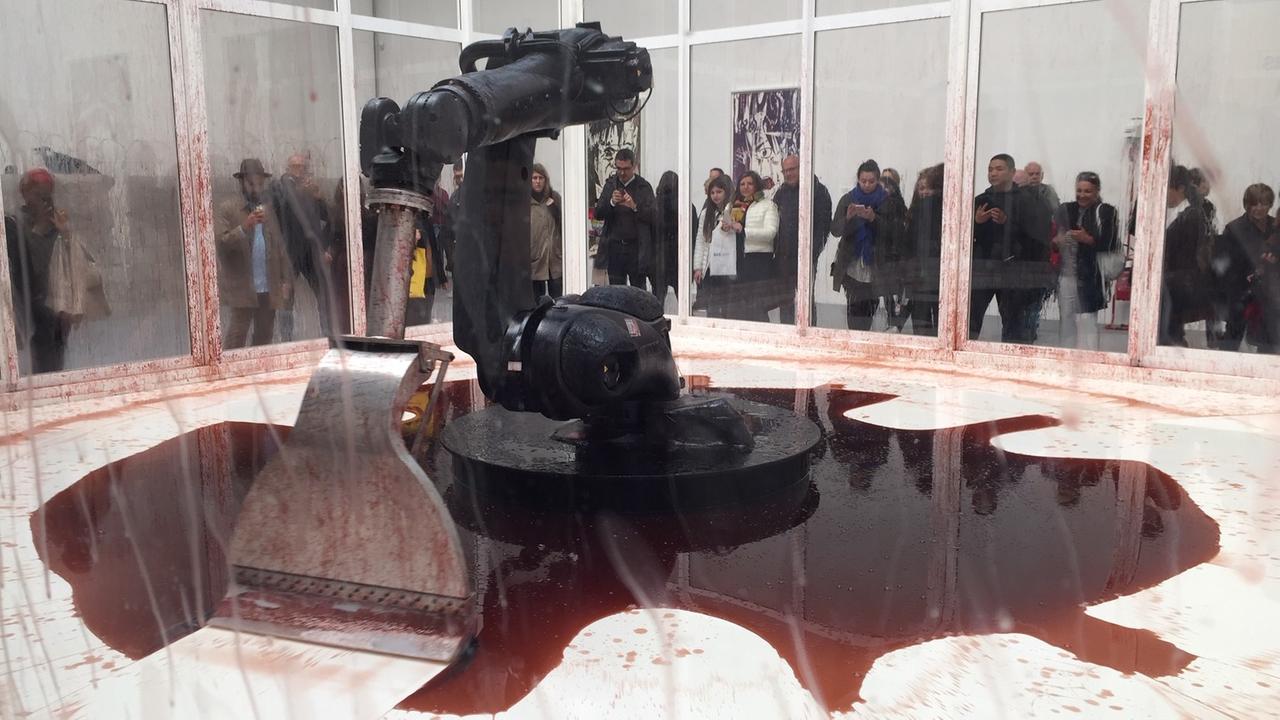 Ein Industrieroboter mit einem spachtelartigen Arm wischt blutrot gefärbtes Wasser immer wieder zu einer Pfütze zusammen. Ein Industrieroboter mit einem spachtelartigen Arm wischt blutrot gefärbtes Wasser immer wieder zu einer Pfütze zusammen.