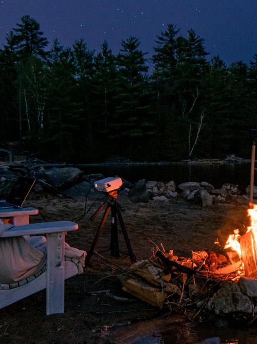 Eine Leinwand, ein Projektor, an einem See mit Lagerfeuer unter dem Sternenhimmel.