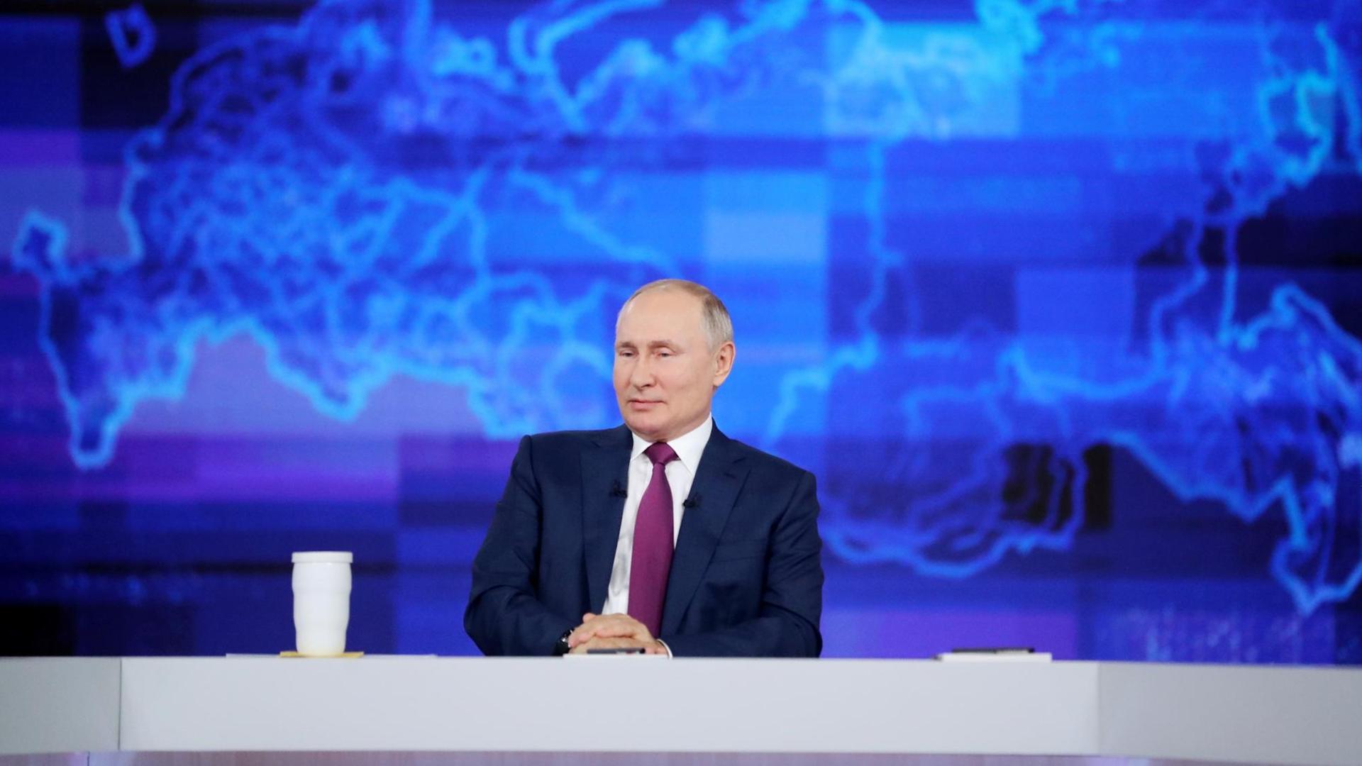 Russlands Präsident Wladimir Putin sitzt in einem Fernsehstudio vor einer blauen Russland-Karte. Russlands Präsident Wladimir Putin sitzt in einem Fernsehstudio vor einer blauen Russland-Karte.