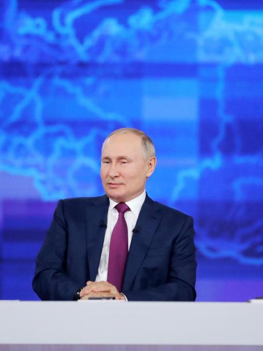Russlands Präsident Wladimir Putin sitzt in einem Fernsehstudio vor einer blauen Russland-Karte.