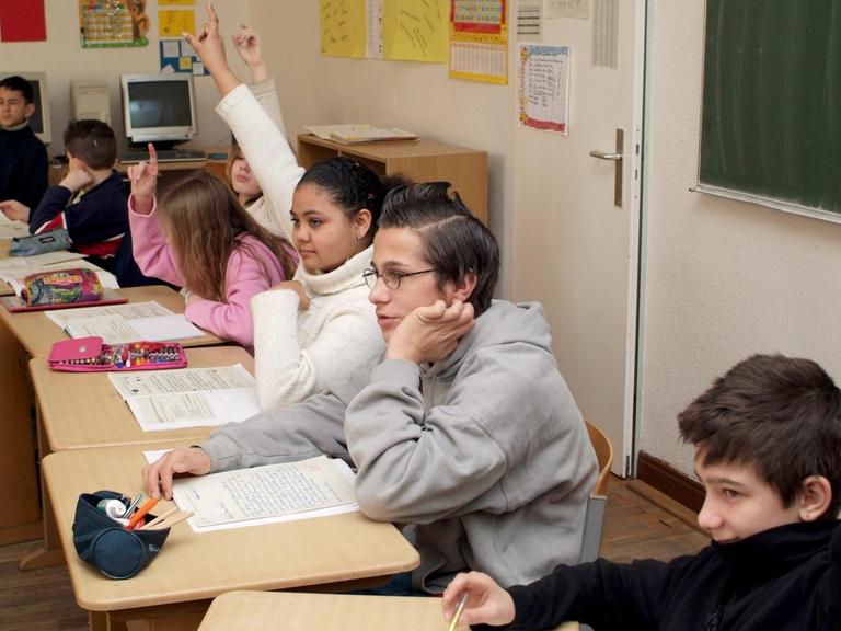 Das Foto zeigt Schüler in ihrem Klassenraum, die sich melden.