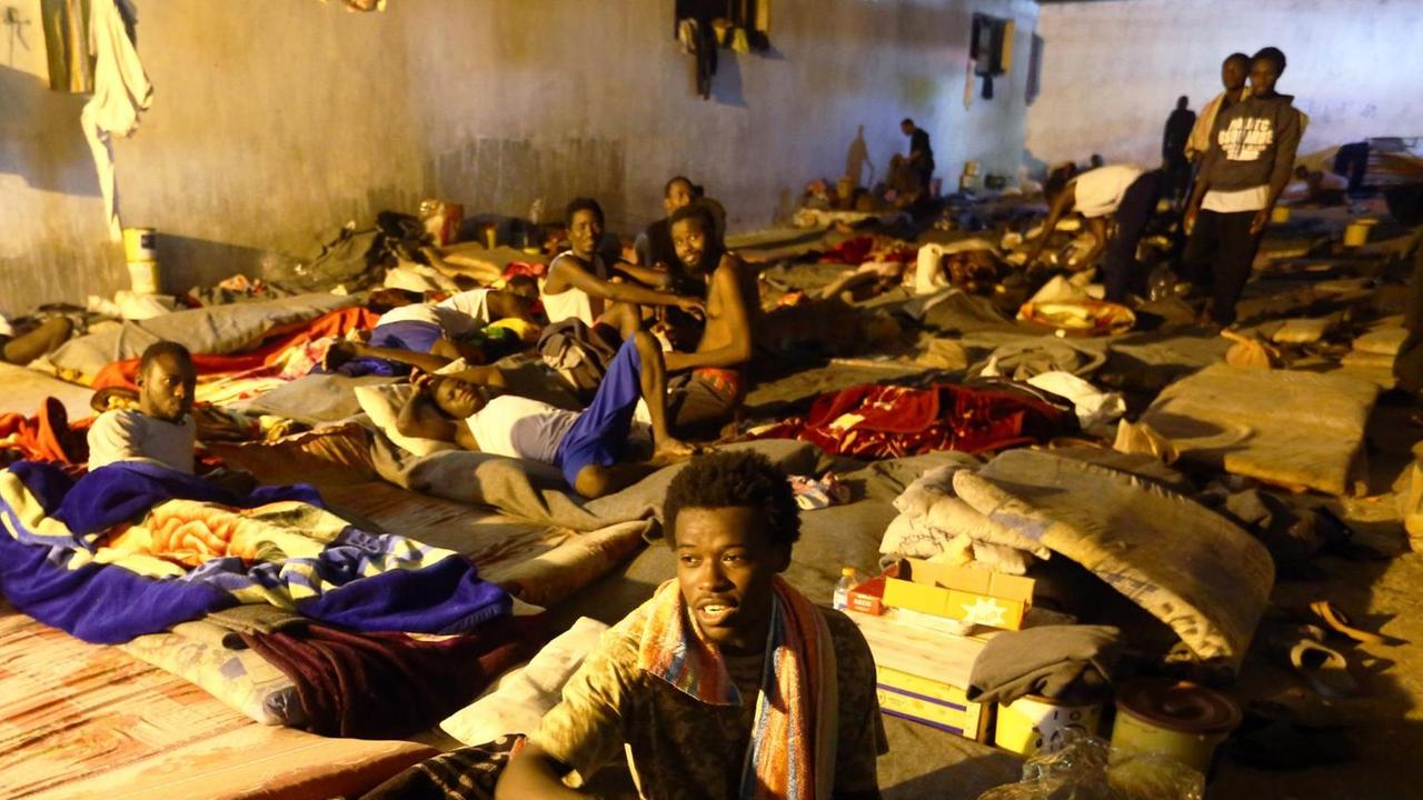 Afrikanische Migranten sitzen auf Decken in einem kahlen Raum Afrikanische Migranten sitzen auf Decken in einem kahlen Raum