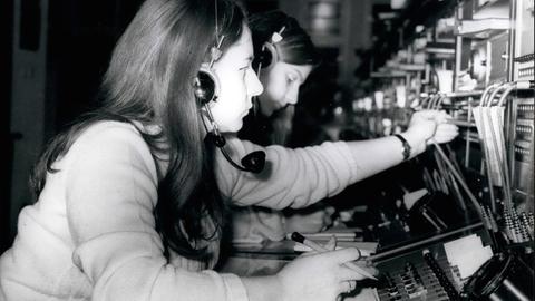 Schwarz-Weiß-Bild: Frauen stecken in Westberlin im Januar 1971 Kabel in Apparaturen, mit deren Hilfe man Telefonvebindungen herstellen kann.