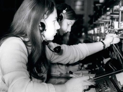 Schwarz-Weiß-Bild: Frauen stecken in Westberlin im Januar 1971 Kabel in Apparaturen, mit deren Hilfe man Telefonvebindungen herstellen kann.