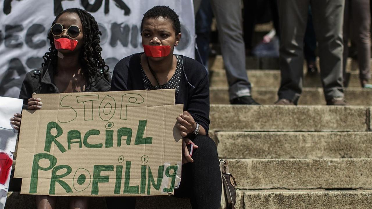 Zwei Schwarze mit rotem Klebeband vor dem Mund halten während einer Demonstration an der Universität von Witwatersrand in Johannesburg, Südafrika, ein Banner mit der Aufschrift "Stop Racial Profiling" hoch.