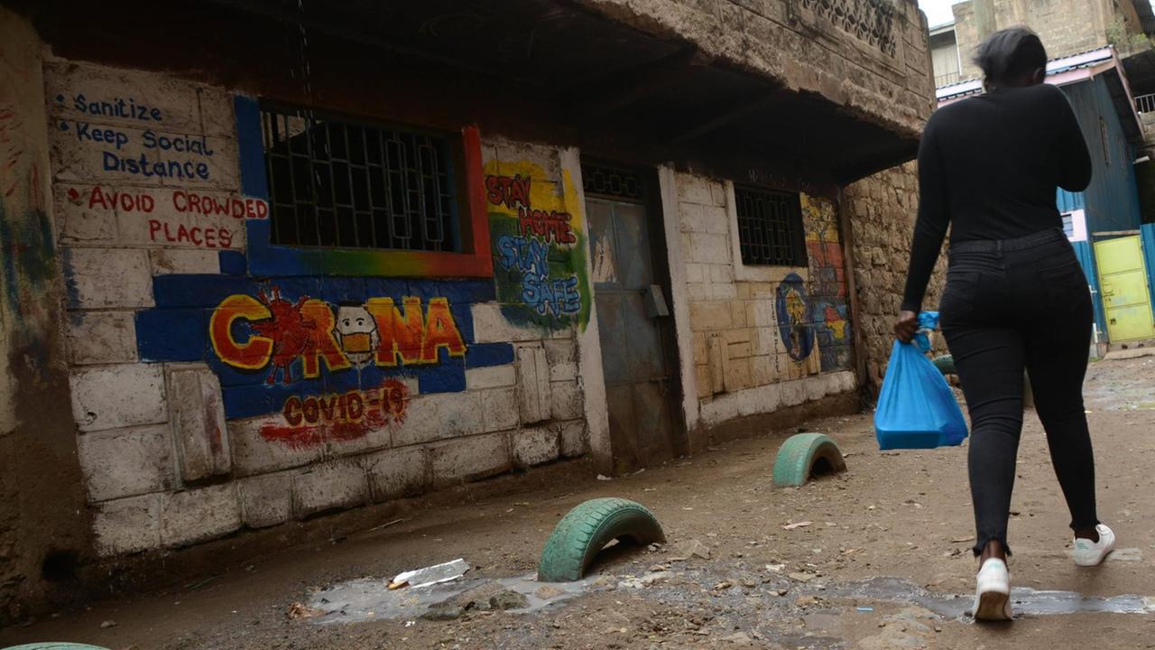 In der kenianischen Hauptstadt Nairobi läuft eine Frau an einem bunten Graffito mit Corona-Verhaltensregeln auf einer Hauswand vorbei.