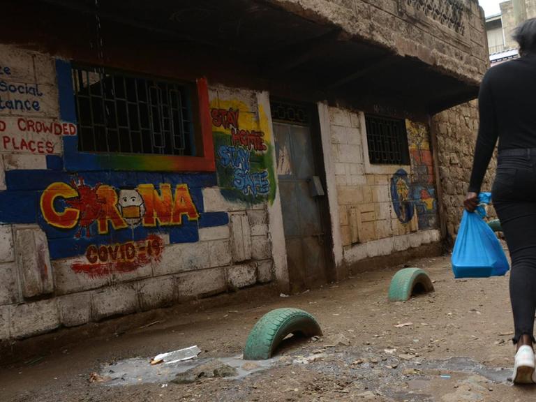In der kenianischen Hauptstadt Nairobi läuft eine Frau an einem bunten Graffito mit Corona-Verhaltensregeln auf einer Hauswand vorbei.