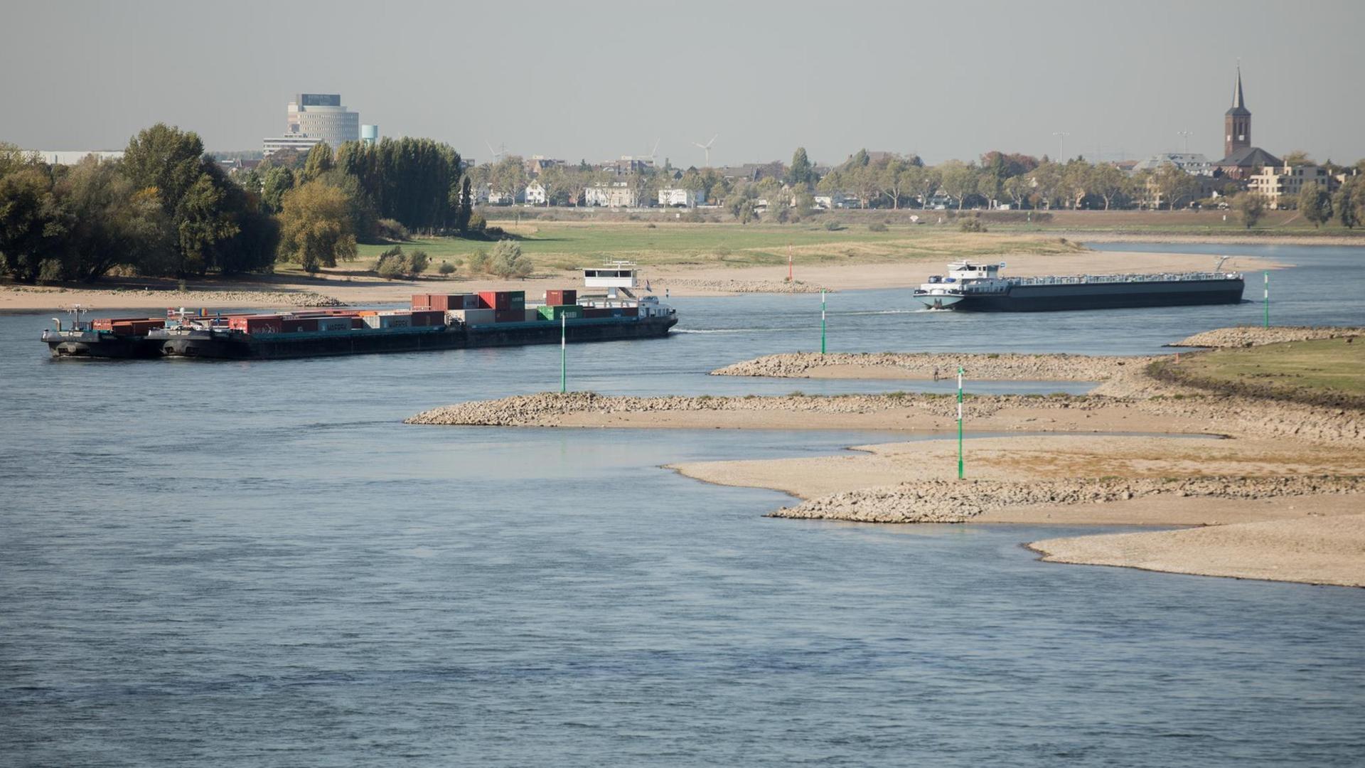 Zwei Schiffe fahren bei Niedrigwasser über den Rhein, zu sehen sind auch Sandbänke, die aus dem Wasser ragen.