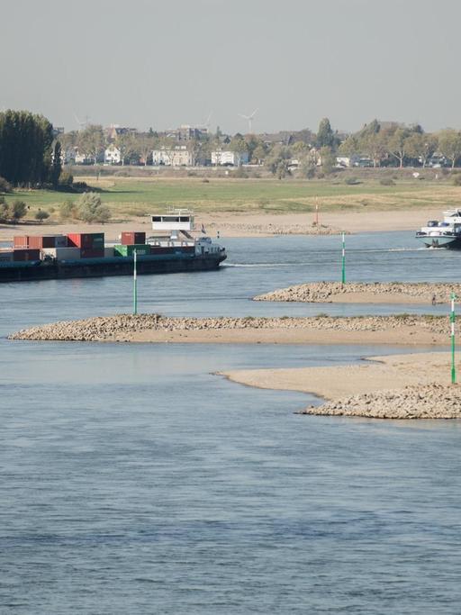 Zwei Schiffe fahren bei Niedrigwasser über den Rhein, zu sehen sind auch Sandbänke, die aus dem Wasser ragen.