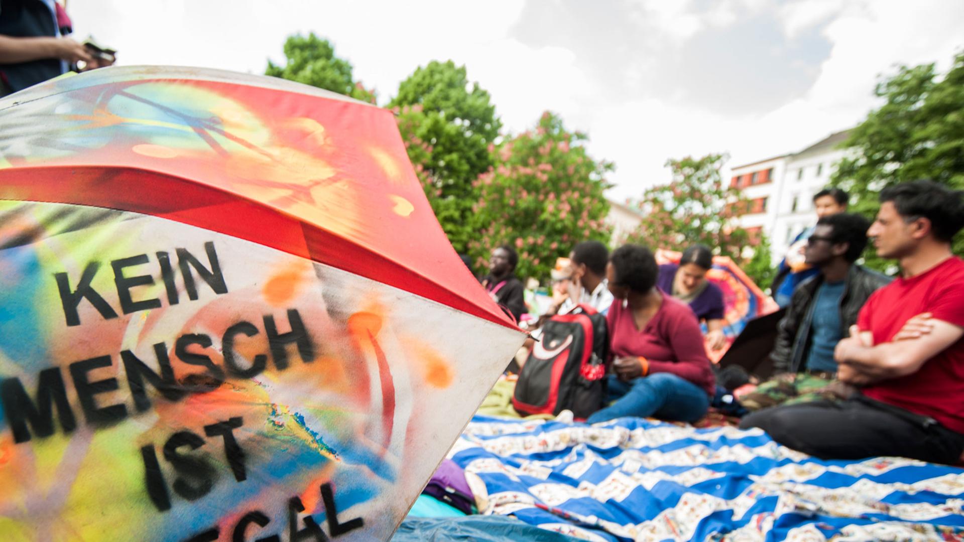 Ein Regenschirm mit der Aufschrift "Kein Mensch ist illegal" liegt am 30.04.2014 bei einer Pressekonferenz auf dem Oranienplatz in Berlin. Die Flüchtlinge und Aktivisten auf dem Berliner Oranienplatz haben ihren Hungerstreik nach einem Gespräch mit der Bundesbeauftragten für Flüchtlinge, Özugus, unterbrochen. Ein Regenschirm mit der Aufschrift "Kein Mensch ist illegal" liegt am 30.04.2014 bei einer Pressekonferenz auf dem Oranienplatz in Berlin. Die Flüchtlinge und Aktivisten auf dem Berliner Oranienplatz haben ihren Hungerstreik nach einem Gespräch mit der Bundesbeauftragten für Flüchtlinge, Özugus, unterbrochen.